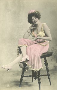 Actrice, avec un joli sourire, en robe rose assise sur un tabouret
